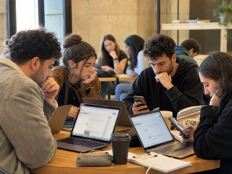 צעירים סביב מחשבים וטלפונים במרחב לימודי, שוקלים תגובה מקוונת בדיון פוליטי.